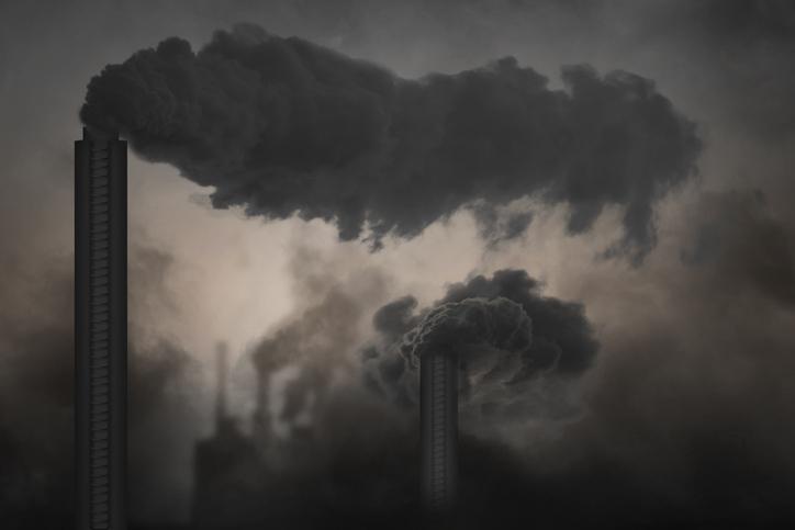 Useita tehtaanpiippuja, joista tupruaa tummaa savua. Koko kuva harmaana savusta.