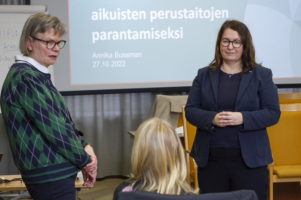 Kaksi seminaarin puhujaa seisovat salin etuosassa ja keskustelevat kolmannen yleisössä istuvan henkilön kanssa.