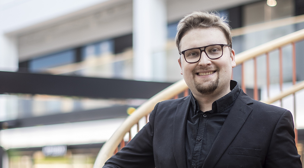 Niku Hinkka hymyilee, taustalla näkyy portaiden kaidetta ja ostoskeskusta.