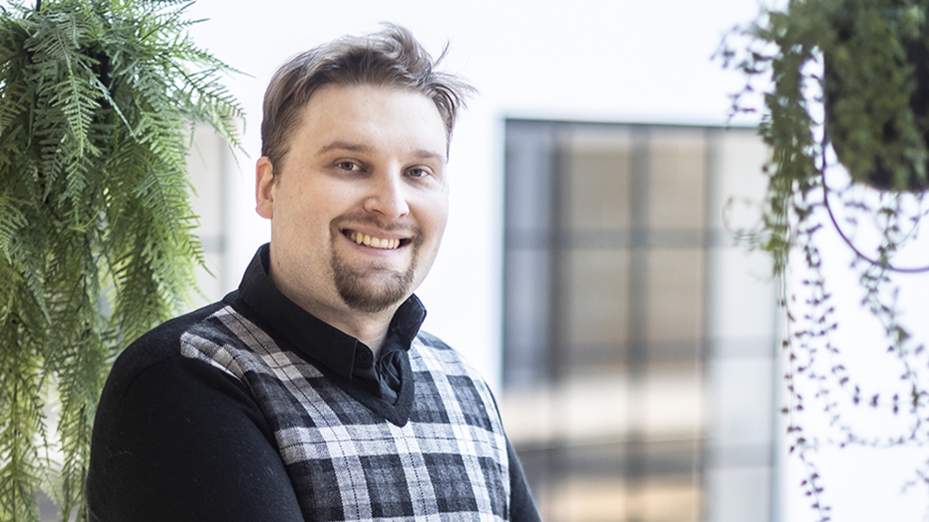 Niku Hinkka hymyilee, taustalla näkyy ikkunoita ja kasveja amppeleissa.