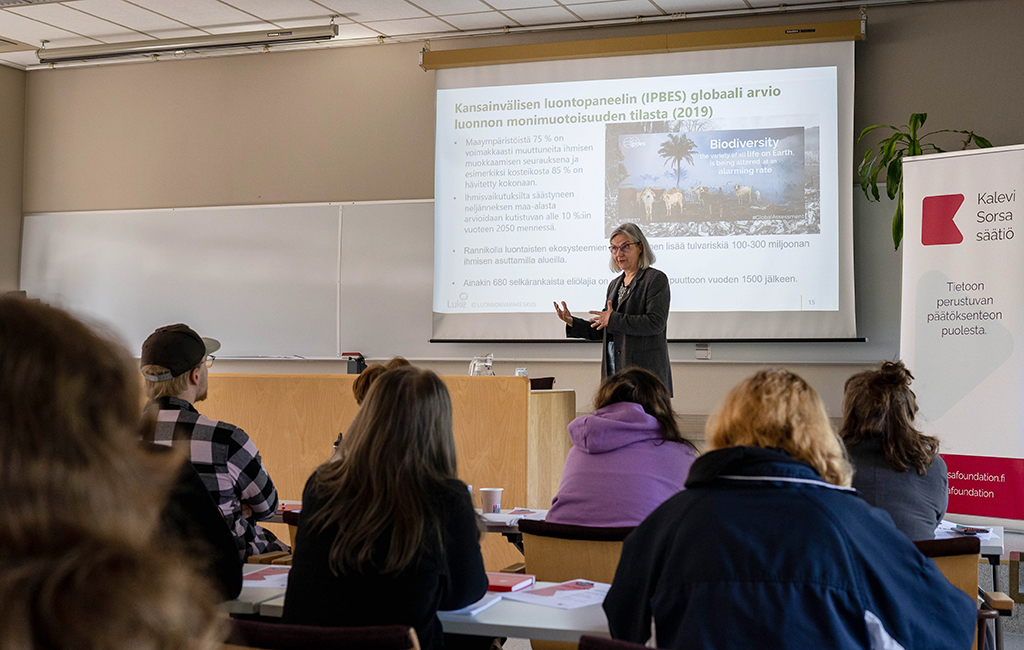 Asiantuntija esiintyy luokkatilan edessä yleisö istuu pulpeteissa ja kuuntelee.