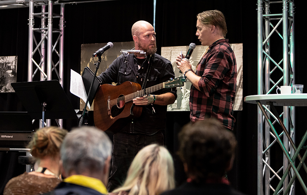 Kaksi miestä keskustelee. Toisella on kitara kädessä.