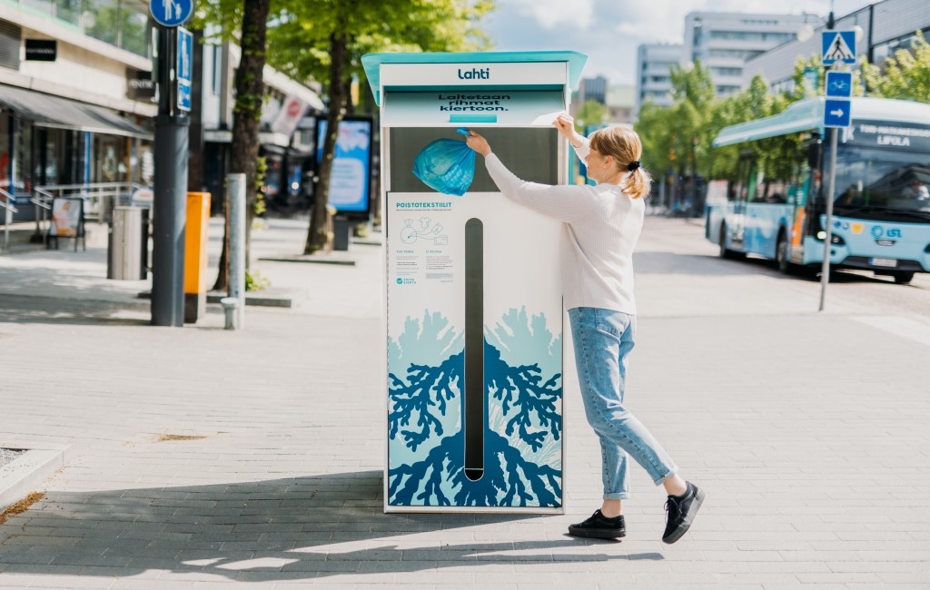 Nainen heittää poistovaatepussia kierrätyslaatikkoon.