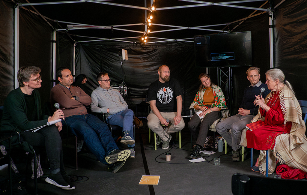 Seitsemän asiantuntijaa keskustelee esiintymislavalla.