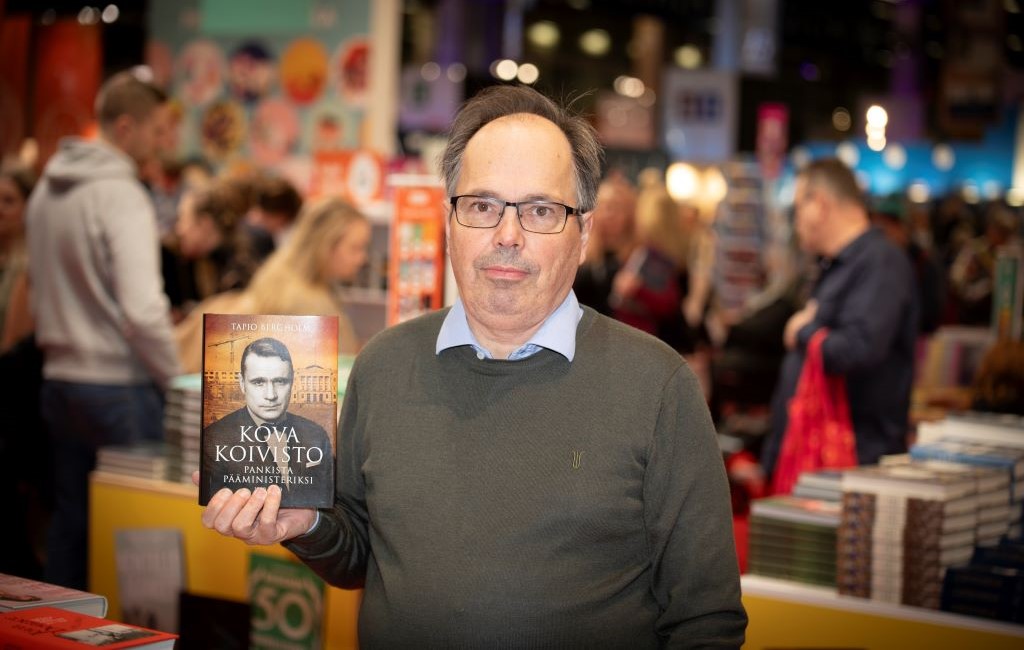 Mies seisoo kirjakaupassa kirja kädessä.