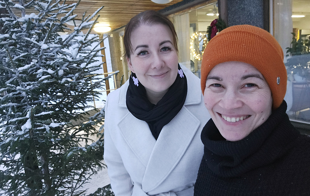 Kaksi naista hymyilee ulkona.