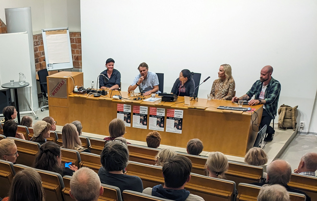 Viisipanelistia keskustelee yleisön edessä.